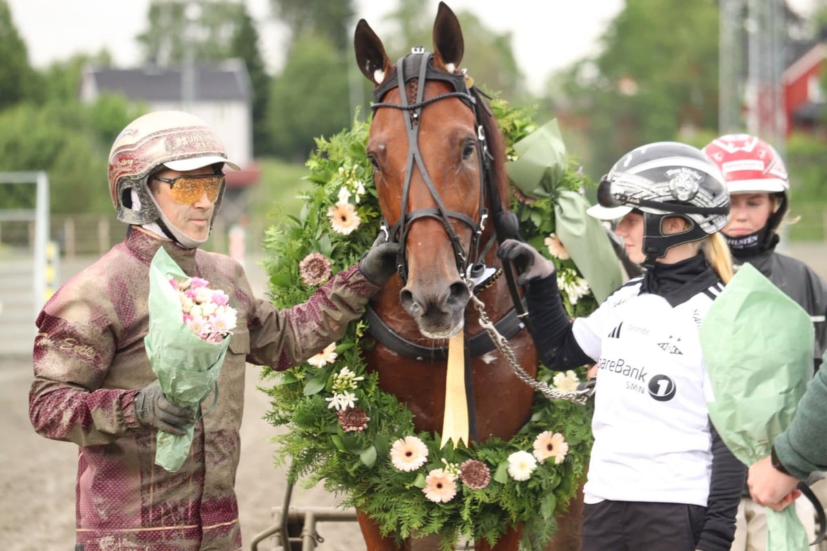 Jockey in pink silks with horse adorned with floral garland, attended by handlers in helmets at equestrian event